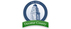 A circular logo featuring a clock tower in the center, with the text "Est. 1850" at the top and a green ribbon at the bottom displaying "Decatur County.
